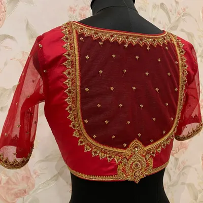 This red blouse features a classic U-shaped back design, framed with heavy zardosi embroidery on a sheer net panel for a regal and elegant look.