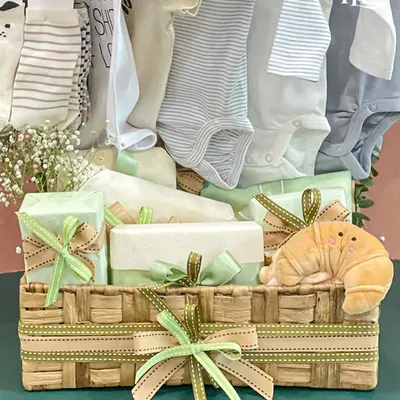 This charming hamper is packed in a woven jute basket and filled with soft, neutral-toned baby clothes and essentials. The plush croissant toy adds a touch of whimsy.