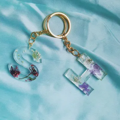 A beautiful pair of floral initial keychains, 'S' and 'H', made with different types of real pressed flowers. This shows how I can create a coordinated set for friends or couples, each with its own unique floral design.
