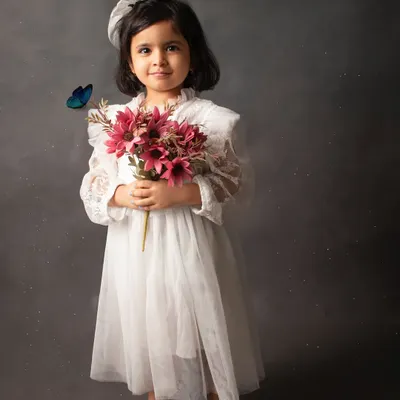 A timeless portrait in a beautiful white lace dress against a classic mottled grey backdrop. The added butterfly gives it a touch of magic.