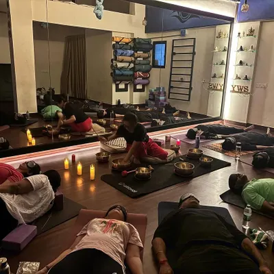 A wide view of a group sound bath, showing participants in a state of deep rest. The room is filled with the warm glow of candles, creating a perfect environment for healing and letting go.