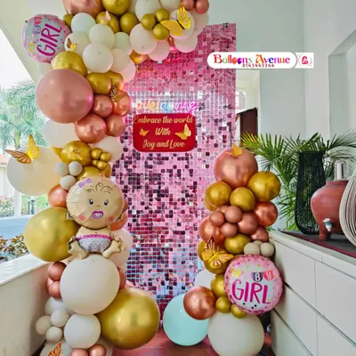 A full view of the pink shimmer wall setup for a baby girl celebration, complete with "It's a Girl" foil balloons.