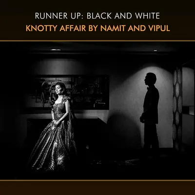 This award-winning black and white photograph is a study in light and shadow. The dramatic lighting creates a moody, cinematic feel, highlighting the bride's stunning gown and the groom's silhouette.