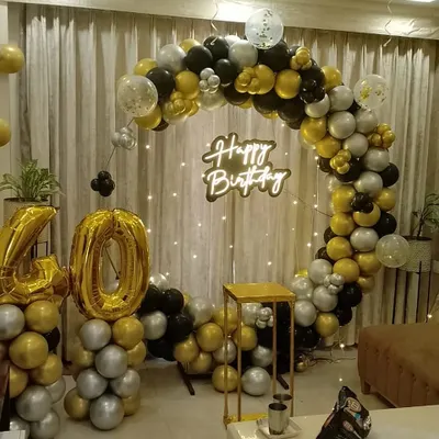 A stylish 40th birthday celebration at home. This setup features a circular balloon arch in black, gold, and silver, a 'Happy Birthday' neon sign, and large '40' foil balloons.