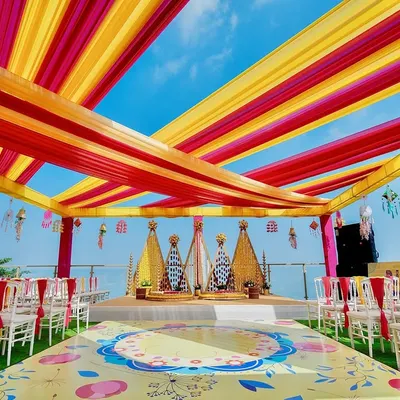 A vibrant Haldi ceremony set against a stunning seaside backdrop. We used bright yellow and pink fabric drapes to create a festive canopy, with a custom-printed floor and floral arrangements that make for incredible photos and an even better experience.
