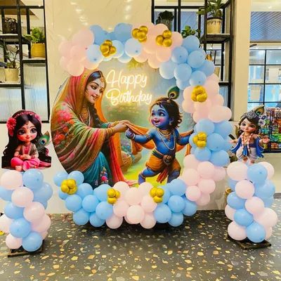 A custom Krishna-themed decoration featuring a circular backdrop with traditional artwork and a surrounding balloon arrangement. This setup is a popular choice for a baby's naming ceremony or first birthday party.