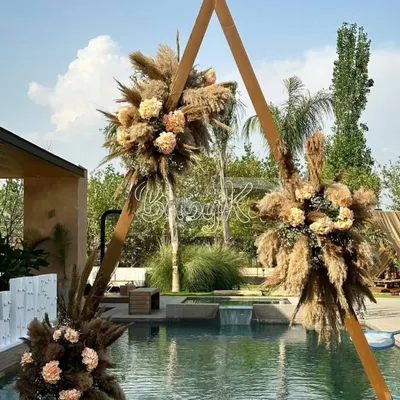This boho-chic baby shower setup was created by the poolside. The triangular wooden arch adorned with pampas grass and a custom name sign made for a stunning and on-trend focal point.