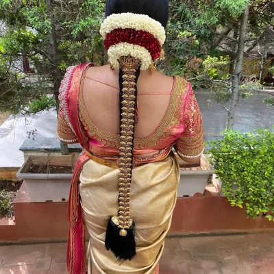 A classic Muhurtham look featuring a long, neat braid decorated with a full set of traditional gold temple jewellery. The base is adorned with a layer of jasmine and red flowers for a vibrant, customary finish.