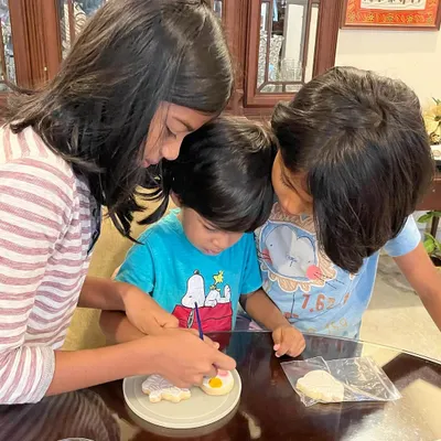 It's so lovely to see siblings getting creative together. This little one is getting some help from his big sisters to paint his cookie. It’s a perfect, screen-free activity for the whole family to enjoy.
