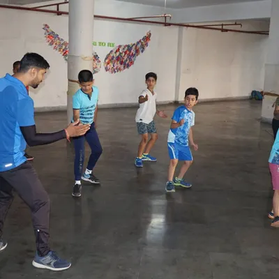 A coach guiding young beginners through their first footwork drills at our summer camp. We focus on making the first experience with fencing fun and engaging.