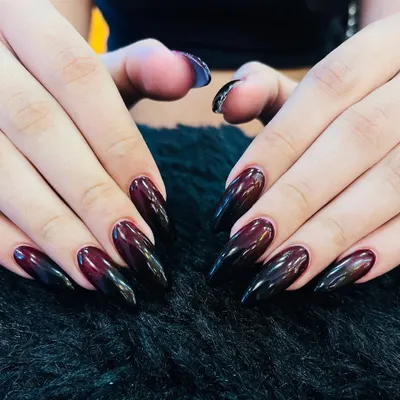 A dark and dramatic ombre effect. These long, almond-shaped nails transition from a deep burgundy at the base to a solid black at the tip, creating a moody and sophisticated look.