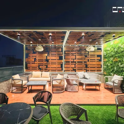 A closer look at our rooftop lounge design, focusing on the main seating area. The combination of a wooden deck, a vertical green wall, and a slatted wood feature wall creates a rich, textured environment. The comfortable sofas and ambient pendant lights make it an inviting space for evening conversations.
