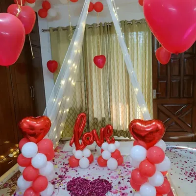 A classic red and white romantic room decoration. I created a beautiful canopy with fairy lights over the bed, flanked by balloon pillars and a "LOVE" message, with a heart made of rose petals as the centerpiece.
