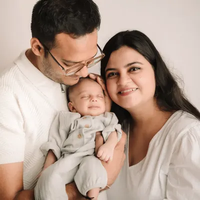 A perfect family portrait with a smiling newborn held lovingly by his parents. The simple white background keeps the focus on them.