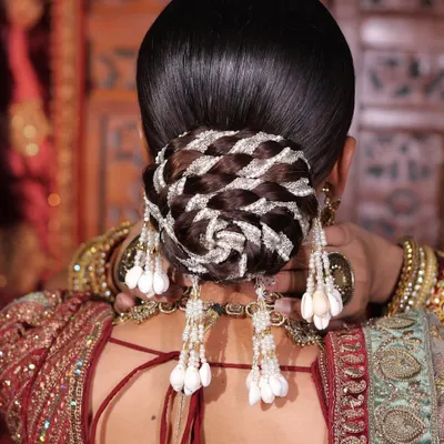 A stunningly intricate bridal bun. This hairstyle features detailed weaving and is accessorized with beautiful hanging shell tassels for a unique, modern touch.