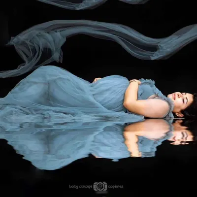 An artistic fine art portrait showing an expecting mother in a dusty blue gown, lying on a reflective surface. The composition creates a stunning mirror image, highlighting the serene beauty of pregnancy.