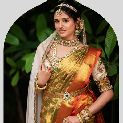 A vision of bridal splendor in an olive green and mustard Kanjeevaram silk saree. The ensemble is completed with a custom embroidered blouse, layered temple jewelry, and a delicate sheer veil for a touch of modernity.