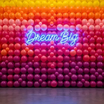 A full-scale balloon wall creates an unforgettable photo opportunity. This design features a warm color gradient from yellow to magenta, centered with an inspiring "Dream Big" neon sign.