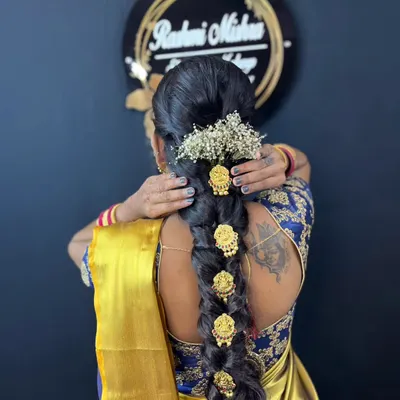 A detailed view of a traditional South Indian bridal hairstyle, featuring a long braid decorated with intricate gold accessories and fresh baby's breath flowers.
