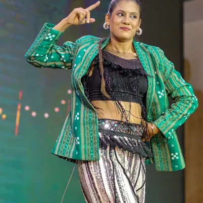 A dynamic pose during a performance that fuses modern dance with Odia cultural elements. The green Sambalpuri jacket adds an authentic touch to the contemporary outfit.