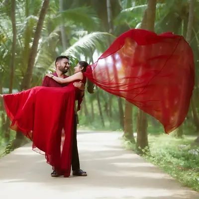 A classic romantic pre-wedding pose with the groom lifting the bride, her vibrant red gown flowing in the wind. This shot, set against a backdrop of palm trees, is perfect for creating a dramatic and memorable image.