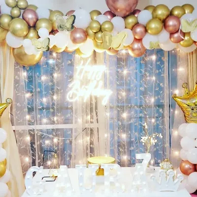 A royal princess theme for Gaura's 7th birthday. The decor includes white and gold balloon columns topped with crowns, a 'Happy Birthday' neon sign, and a matching balloon garland.