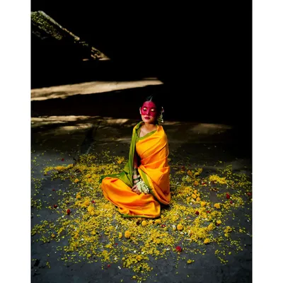 An artistic interpretation of the Haldi ceremony. The dramatic lighting, vibrant yellow saree, and scattered flowers create a powerful, conceptual image that tells a cultural story.
