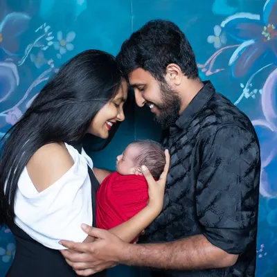 New parents share a happy, intimate moment, their foreheads touching as they cradle their newborn wrapped in a bright red swaddle.