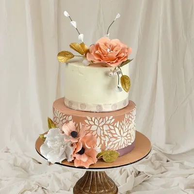 This two-tiered cake is a study in elegance, combining delicate stencil work on the bottom tier with beautiful, handcrafted sugar flowers on top.