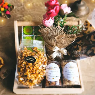 Our Floral Indulgence Gourmet Hamper is curated to delight all senses. It includes caramel popcorn, jars of roasted nuts, handcrafted chocolates, and a rustic mini bouquet, all arranged in a charming wooden crate.
