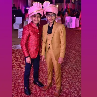 Custom ethnic wear isn't just for adults. Here are two young clients looking smart in their tailored outfits, a red brocade Jodhpuri jacket and a tan three-piece suit, for a family wedding.