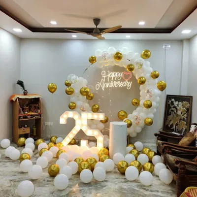 This elegant 25th-anniversary decoration in a home setting shows a complete package. It includes a white and gold balloon ring, a "Happy Anniversary" neon sign for a warm glow, and large light-up "25" numbers that serve as a fantastic centerpiece.