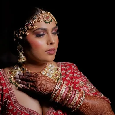 A stunning bridal portrait against a black background. The bride's intricate jewelry, henna, and confident pose are highlighted beautifully.