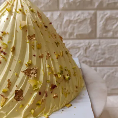 A close-up of my special Modak Cake, created for Ganesh Chaturthi. It’s a vanilla cake filled with coconut-jaggery saran, frosted beautifully, and garnished with pistachios and gold leaf.