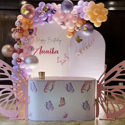 A magical butterfly theme for Anaika's birthday. The setup includes a custom-printed cake table, large pink butterfly wing cutouts, and a pastel balloon arch with delicate butterfly accents.
