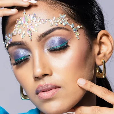 A detailed beauty close-up showcasing iridescent face gems on the forehead and vibrant purple and blue eyeshadow. This type of shot is ideal for a makeup artist's portfolio or a beauty editorial.