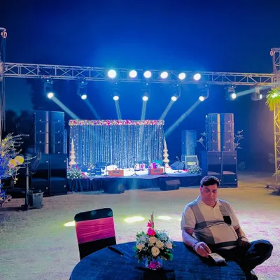 A professional stage setup for a sangeet or music night. This includes a full truss system with spotlights, powerful speakers, and a decorated backdrop for the performers.