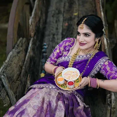A beautiful portrait for Sankranti, with the model in a traditional purple half saree, holding a plate of offerings. The rustic bullock cart adds a classic touch.