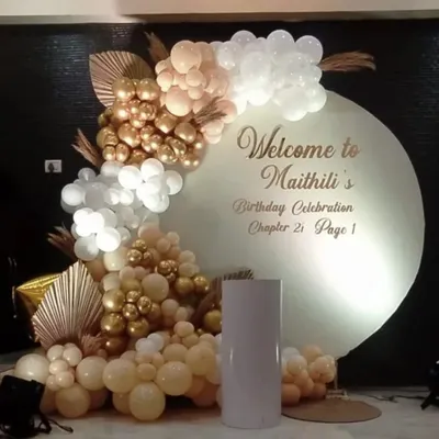 A sophisticated welcome backdrop for a 21st birthday. This setup features a personalized circular board and an organic balloon garland in a chic palette of white, beige, and chrome gold.