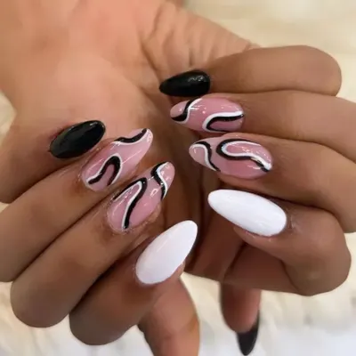 A trendy and artistic manicure featuring abstract designs. This set combines solid black and white nails with accent nails that have a nude base and bold, free-flowing black and white swirls.