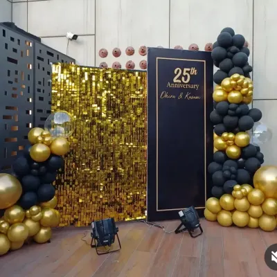 A sophisticated black and gold backdrop for a 25th anniversary party. This setup features a gold sequin panel, a personalized sign, and dramatic balloon garlands, all highlighted with professional spotlights.