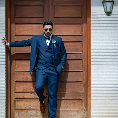 A groom with style. This portrait captures a cool, confident look as he leans against a rustic wooden door, ready for the big day.