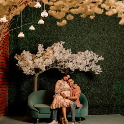 A wide shot from a styled maternity session, showing the couple seated under a canopy of lights and blossoms. This demonstrates a more creative and decorative approach to maternity photography.