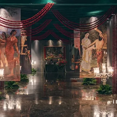 The grand entrance to our Raja Ravi Varma-inspired sangeet. Guests walk through a gallery of the artist's iconic paintings, printed on large scrolls and flanked by candelabras, setting a dramatic and artistic tone for the evening.