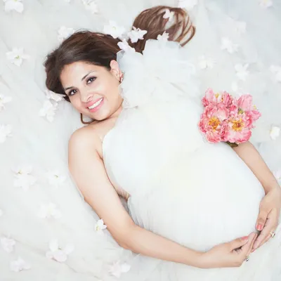 A dreamy top-down shot creating an ethereal feel. The mother-to-be is surrounded by soft white fabric and flowers, resulting in a peaceful and artistic maternity photograph.
