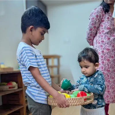 This heartwarming moment shows an older sibling, a Hastam alumnus, helping his younger sister with a basket of play vegetables on her first day. It is a perfect example of the caring and supportive peer relationships that flourish in our school.