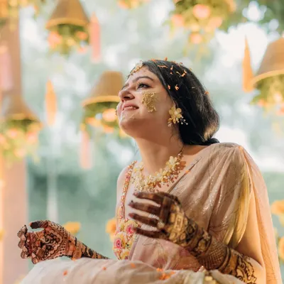 A moment of pure bliss during the Haldi ceremony. The bride, adorned with turmeric and flower petals, looks up with a joyful smile, perfectly capturing the spirit of the celebration.