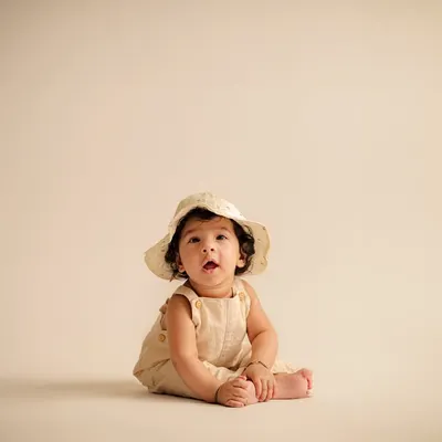 A perfect sitter session portrait. At six months, babies can often sit up unassisted, and we capture their proud smiles with simple props like this cute hat.