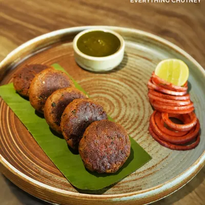 Our Mutton Shikampuri Kebabs are tender, flavorful patties served on a banana leaf. They come with our "everything chutney" and pickled onions, offering a perfect balance of spice and tang in every bite.