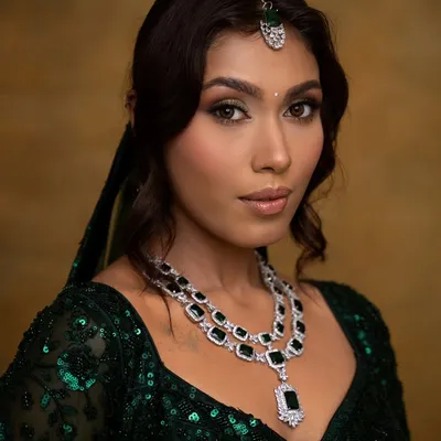 A regal and elegant look featuring a shimmery green and gold eye makeup. This look was designed to complement the emerald green lehenga and diamond jewelry, perfect for a bride's reception or sangeet.